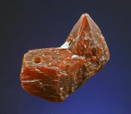 Zincite, Franklin, New Jersey. An outstanding crystal of zincite from Franklin. It was acquired from the family of a Keweenaw copper miner who had used it for years as a watch fob (the hole drilled to accommodate this usage is visible on the left side of the specimen in the photo).  Specimen 3 cm wide.Photo by G. Robinson. (DM 30818) 